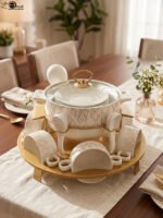 Ceramic soup tureen set with glass lid, matching double-handled bowls, saucers, spoons, and a gold metal warming stand on a dining table setting.