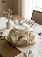 Luxury white ceramic soup tureen set with gold leaf pattern on a metal buffet burner stand with matching bowls and spoons.