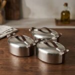 Set of three brushed stainless steel insulated hot pots with leather-look handles on a wooden table