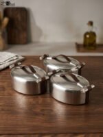 Set of three brushed stainless steel insulated hot pots with leather-look handles on a wooden table