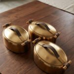 3-piece luxury brushed gold oval insulated hot pot set with leather accent handles displayed on a wooden dining table