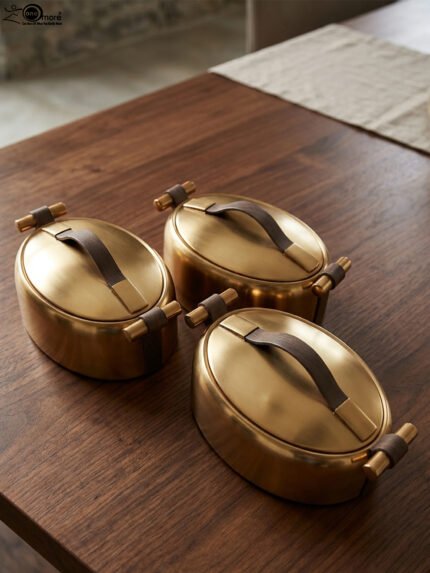 3-piece luxury brushed gold oval insulated hot pot set with leather accent handles displayed on a wooden dining table