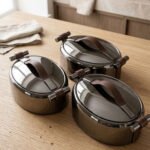 One More 3-piece gunmetal stainless steel insulated hot pot set with wood-grain handles on a wooden table.