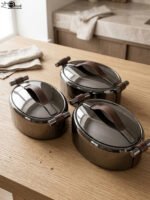 One More 3-piece gunmetal stainless steel insulated hot pot set with wood-grain handles on a wooden table.