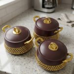 Set of three deep maroon insulated hot pots with gold handles and honeycomb gold accent trim on a kitchen counter.