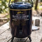 Day Days 9.5 Liter dark blue insulated water cooler jug with spigot tap and tripod legs set on an outdoor picnic table.