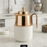 One More 1 Liter white fluted thermal flask with a polished rose gold lid, spout, and ergonomic handle on a kitchen countertop.