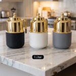 Three One More 1 liter luxury thermal vacuum flasks in black, white, and grey with polished gold tops on a marble kitchen countertop.