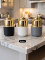 Three One More 1 liter luxury thermal vacuum flasks in black, white, and grey with polished gold tops on a marble kitchen countertop.