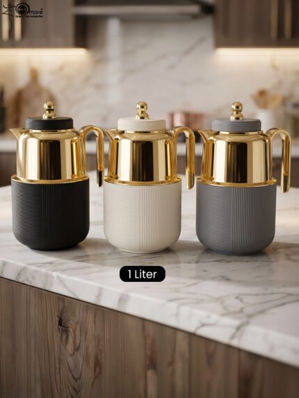 Three One More 1-liter luxury thermal vacuum flasks with polished gold-tone tops and textured ribbed bases in matte black, off-white, and grey resting on a marble kitchen countertop.