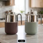 Two One More 1 Liter thermal vacuum coffee carafes in brown and sage green with ribbed bases and polished stainless steel tops on a kitchen counter.