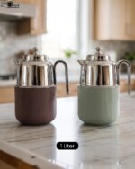 Two One More 1 Liter thermal vacuum coffee carafes in brown and sage green with ribbed bases and polished stainless steel tops on a kitchen counter.