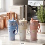 Three 710ml One More VOGUE aesthetic water bottles in pastel blue, cream, and pink featuring straw lids, carrying straps, and floral prints on a kitchen counter.