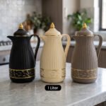 Three ONE MORE 1-liter ribbed luxury vacuum flasks in black, cream, and taupe with gold top finials on a marble kitchen counter.
