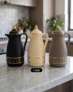 Three ONE MORE 1-liter ribbed luxury vacuum flasks in black, cream, and taupe with gold top finials on a marble kitchen counter.