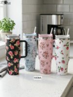 Four 1180ml floral printed insulated tumblers with handles and reusable straws standing on a kitchen counter.