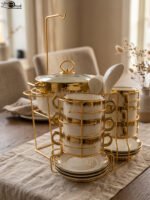 White ceramic soup tureen and stacked double-handled soup bowls with gold rim accents on a gold wire stand on a dining table.