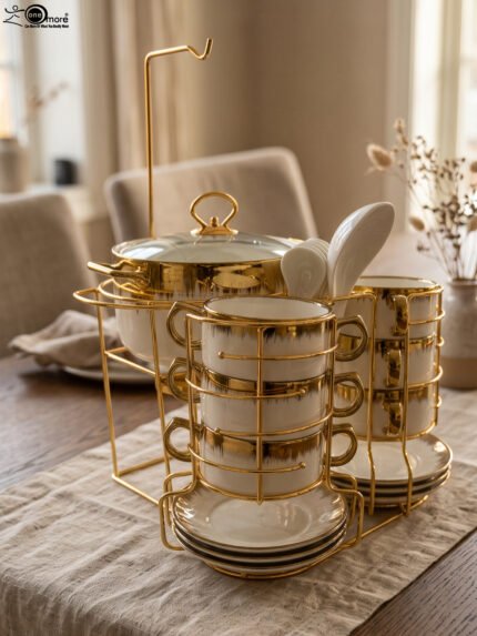 White ceramic soup tureen and stacked double-handled soup bowls with gold rim accents on a gold wire stand on a dining table.