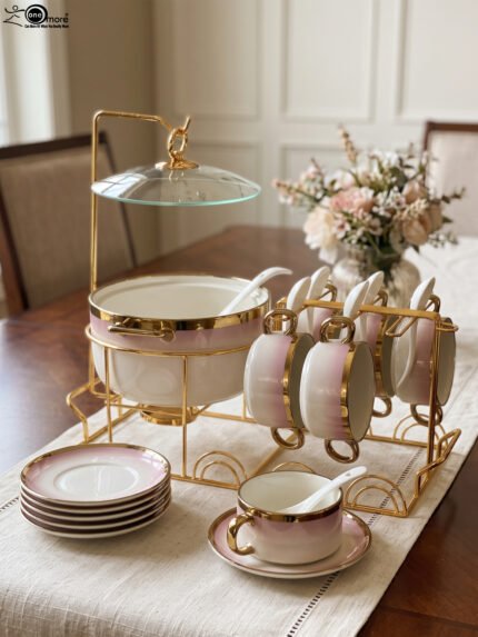 Pink and white gradient ceramic soup tureen set with gold rims, suspended glass lid on a gold frame, buffet burner warmer stand, matching soup cups, saucers, and ceramic spoons.