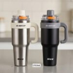Two HI-HOTCUP 1250ml stainless steel insulated tumblers with handles in silver-cream and matte black on a kitchen counter.