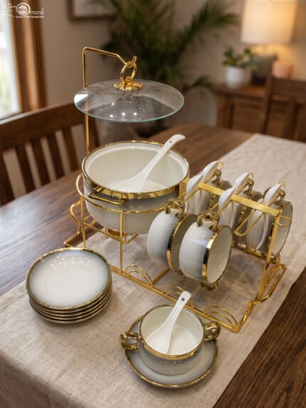 Luxury white ceramic soup tureen set with gold accents, hanging glass lid, matching soup bowls, saucers, and spoons on a gold metal stand.