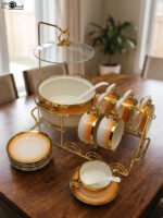 Ceramic soup tureen set with orange gradient rims and gold accents, including hanging soup cups, saucers, and spoons organized on a gold metal rack.