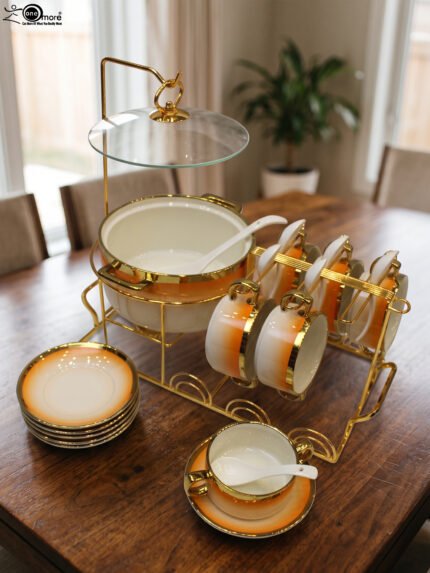 Ceramic soup tureen set with orange gradient rims and gold accents, including hanging soup cups, saucers, and spoons organized on a gold metal rack.