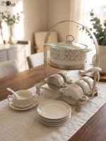 Luxury ceramic soup tureen set featuring a patterned soup pot, soup bowls with handles, matching saucers, spoons, and a gold metal stand on a wooden dining table.
