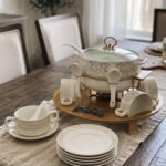 Luxury white ceramic soup tureen set with gold leaf pattern on a metal buffet burner stand with matching bowls and spoons.