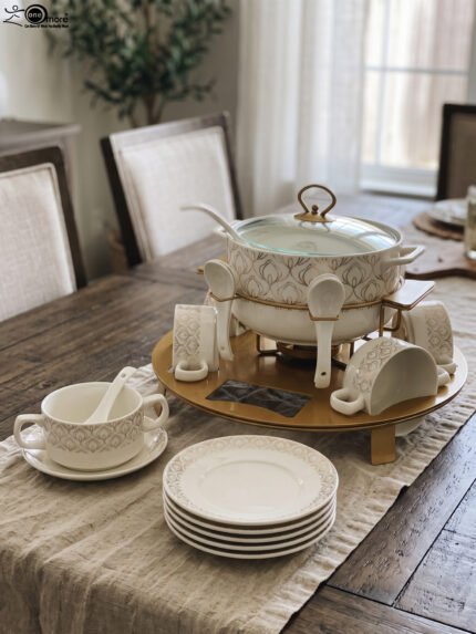 Luxury white ceramic soup tureen set with gold leaf pattern on a metal buffet burner stand with matching bowls and spoons.