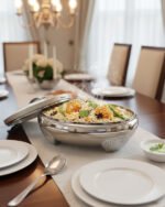 Cream and stainless steel insulated thermal hotpot casserole dish with lid resting on a granite kitchen countertop.