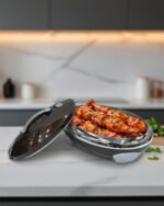 An elegant oval-shaped insulated hotpot in dark brown with a silver stainless steel interior and decorative studded handles, open with the lid resting on a polished wooden dining table.