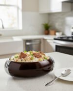 Glossy brown oval insulated hotpot casserole with chrome handle on a modern kitchen countertop.