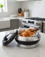 Premium black and silver insulated hotpot casserole dish on an elegantly set wooden dining table with white roses and wine glasses.