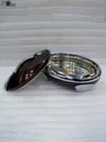 An elegant oval-shaped insulated hotpot in dark brown with a silver stainless steel interior and decorative studded handles, open with the lid resting on a polished wooden dining table.