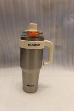 Two HI-HOTCUP 1250ml stainless steel insulated tumblers with handles in silver-cream and matte black on a kitchen counter.