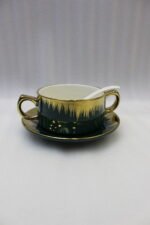 Luxury emerald green ceramic soup tureen set with gold accents, glass lid, warmer stand, stacked double-handled cups, saucers, and white spoons on a marble countertop.