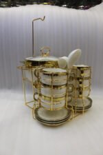 White ceramic soup tureen and stacked double-handled soup bowls with gold rim accents on a gold wire stand on a dining table.