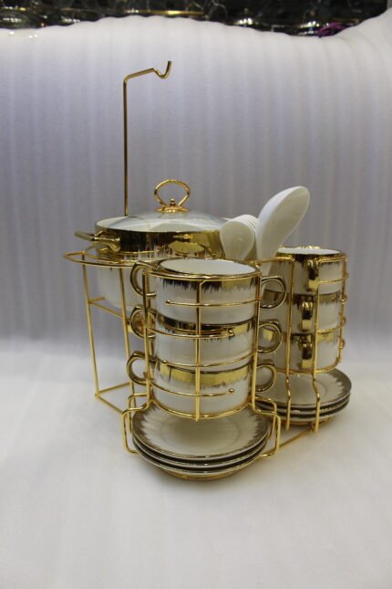 White ceramic soup tureen and stacked double-handled soup bowls with gold rim accents on a gold wire stand on a dining table.