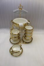 White ceramic soup tureen and stacked double-handled soup bowls with gold rim accents on a gold wire stand on a dining table.