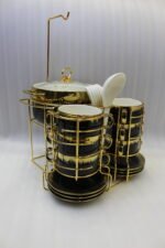 Luxury black and gold ceramic soup set with double-handled cups, covered soup tureen, white spoons, and gold metal display rack on a marble kitchen counter.