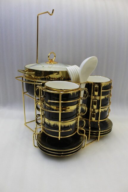 Luxury black and gold ceramic soup set with double-handled cups, covered soup tureen, white spoons, and gold metal display rack on a marble kitchen counter.