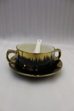 Luxury black and gold ceramic soup set with double-handled cups, covered soup tureen, white spoons, and gold metal display rack on a marble kitchen counter.