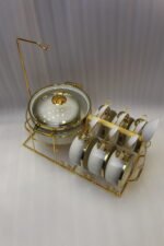 Luxury white ceramic soup tureen set with gold accents, hanging glass lid, matching soup bowls, saucers, and spoons on a gold metal stand.