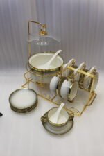 Luxury white ceramic soup tureen set with gold accents, hanging glass lid, matching soup bowls, saucers, and spoons on a gold metal stand.