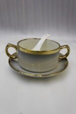 Luxury white ceramic soup tureen set with gold accents, hanging glass lid, matching soup bowls, saucers, and spoons on a gold metal stand.