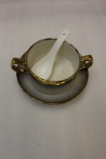 Luxury white ceramic soup tureen set with gold accents, hanging glass lid, matching soup bowls, saucers, and spoons on a gold metal stand.