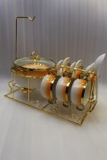 Ceramic soup tureen set with orange gradient rims and gold accents, including hanging soup cups, saucers, and spoons organized on a gold metal rack.