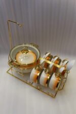 Ceramic soup tureen set with orange gradient rims and gold accents, including hanging soup cups, saucers, and spoons organized on a gold metal rack.