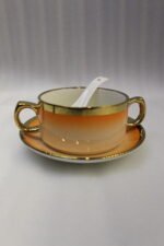 Ceramic soup tureen set with orange gradient rims and gold accents, including hanging soup cups, saucers, and spoons organized on a gold metal rack.